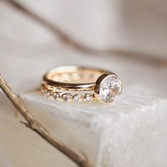 two gold wedding rings sitting on top of a piece of cloth next to a twig