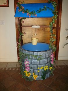 an outdoor fountain with flowers around it and a blue cover over the top that has a bucket in it