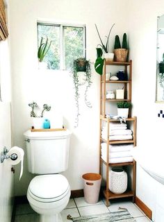 a white toilet sitting next to a bath tub in a bathroom with plants on the shelves