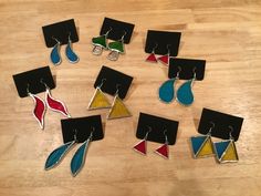 six pairs of earrings are sitting on a wooden surface, each with different shapes and colors