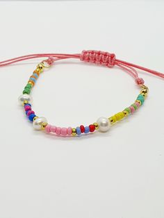 the bracelet is decorated with colorful beads and pearls on a red string that has a gold plated clasp