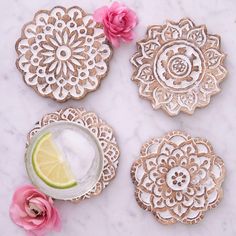 four decorative coasters on a marble surface with pink flowers and a lime slice next to them