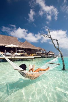 a woman laying in a hammock on the beach reading a book while relaxing