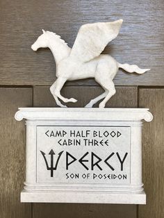 a white horse statue sitting on top of a wooden door frame next to a sign that says camp half blood cabin three victory son of positon