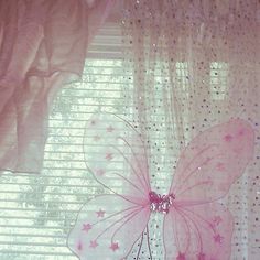 a pink butterfly sitting on top of a window sill next to a white curtain