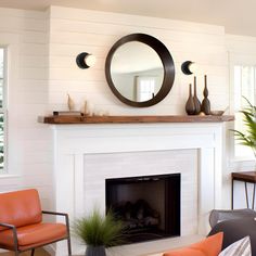 a living room with two chairs and a fire place in front of a mirror on the wall