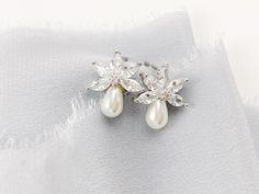 a pair of pearl and crystal earrings on top of a piece of white fabric,