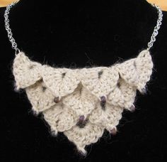 a white crocheted necklace is on a black mannequin neckpiece with silver chains