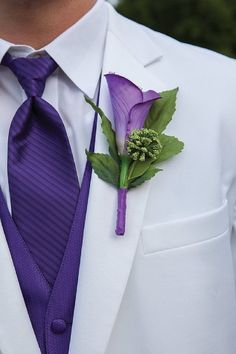 a man in a white suit and purple tie with a flower on his lapel