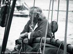 an old woman sitting on the back of a sailboat looking out at the water