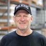 a man wearing a black hat standing in front of a warehouse filled with pallets