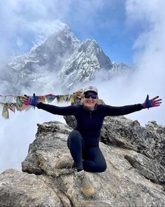 a woman sitting on top of a mountain with her arms spread out in the air