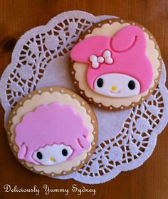 two decorated cookies sitting on top of a doily next to each other, one with a hello kitty face