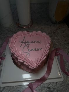 a heart - shaped cake with the words aquarius season written on it and pink ribbon