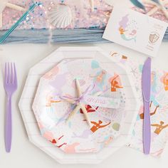 there is a place setting on the table with mermaid paper plates and purple plastic utensils