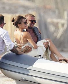 a man and woman sitting on the back of a boat in the sand, with one person holding his arm around the other