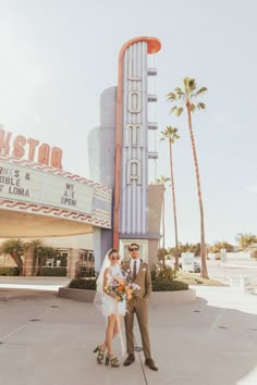 a man and woman standing in front of a movie theater with the marquee behind them