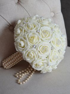 a bridal bouquet with pearls and white roses on a chair in front of a pillow