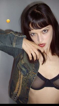 a woman in a black bra and jean jacket posing for the camera with her hand on her shoulder