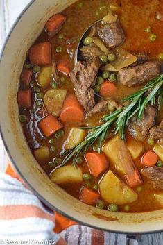 a pot filled with stew and carrots on top of a wooden table next to a striped towel