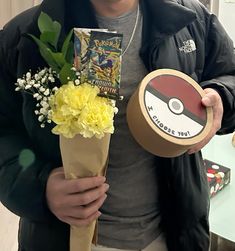 a man is holding a box with flowers and a pokemon card in it, while wearing a hat