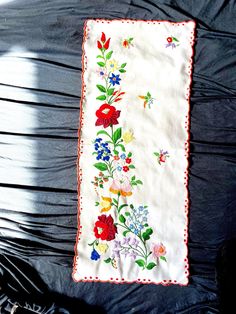 an embroidered cloth with flowers and butterflies is laying on a black tablecloth covered surface