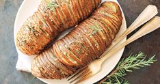 two baked potatoes on a white plate with wooden utensils and rosemary sprigs