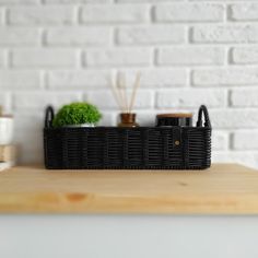 a black basket sitting on top of a wooden table next to a white brick wall