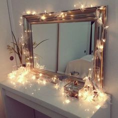 a mirror sitting on top of a white table next to a dresser with lights around it