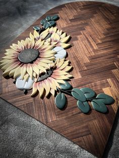 a wooden cutting board with flowers and leaves on the top, along with green stones