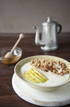 a bowl filled with yogurt, granola and sliced apples on top of a wooden table