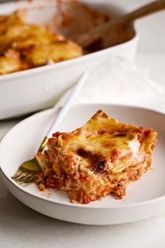 a white plate topped with lasagna next to a casserole dish