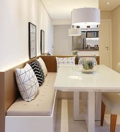 a white table and bench in a small room with light colored walls, flooring and furniture