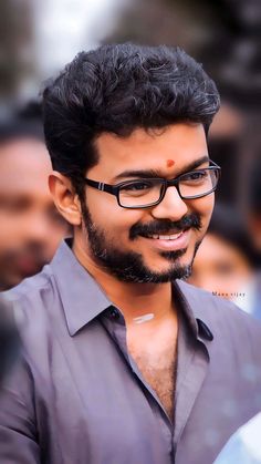 a man with glasses and a beard smiling at the camera while standing in front of other people