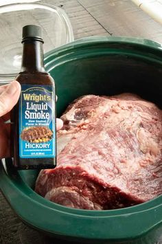 a person holding a bottle of liquid next to a raw meat in a green bowl