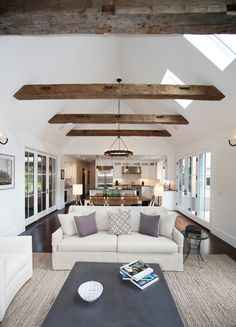 a living room filled with white furniture and lots of wood beamed ceiling beams in an open floor plan