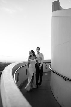 a man and woman standing next to each other on top of a tall building in black and white