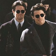 two men in suits and sunglasses are walking down the street with other people behind them