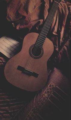 an ukulele sitting on top of a bed next to a book and pen