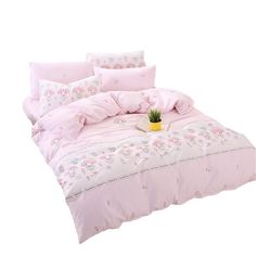 a bed with pink comforters and pillows on top of it, next to a potted plant