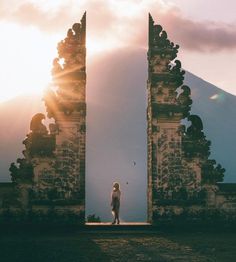 a person standing in front of two stone archways with mountains in the back ground