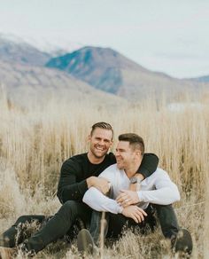 two men sitting on the ground in tall grass with mountains in the backgroud