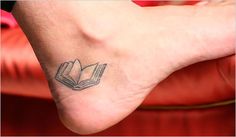 a small tattoo on the foot of a person with a book in it's hand