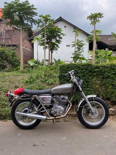 a motorcycle parked in front of a hedge and some houses on the side of the road