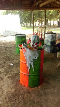 an orange and green barrel with a clown face on it sitting under a covered area