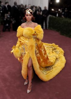 a woman in a yellow gown and fur coat walking down the red carpet at an event