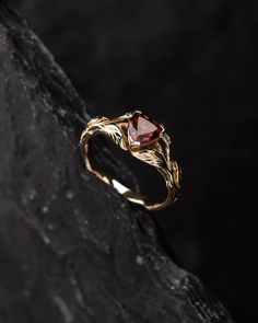 a gold ring with a red stone in the middle on top of a black rock