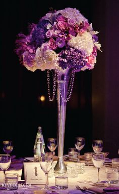 a tall vase filled with purple and white flowers on top of a table next to a bottle