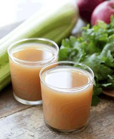 two glasses filled with liquid sitting next to vegetables