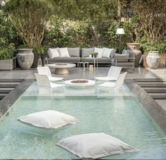 an outdoor living area with couches and pillows on the floor, surrounded by greenery